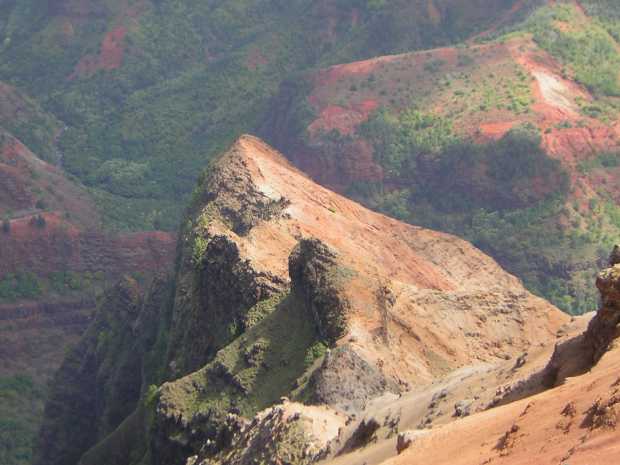A slanted peak, mossy green under shade at left, smooth orange and tan in sun at right, looms close with forested red slopes beyond. A slanted peak, mossy green under shade at left, smooth orange and tan in sun at right, looms close with forested red slopes beyond.