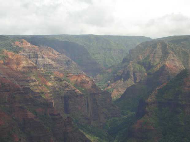 Haze-muted pink and red layered mountains slope downward from left and right, forming a series of V-shaped gorges marching in zigzag order off into the distance. Haze-muted red layered mountains slope downward from left and right, forming a series of V-shaped gorges marching in zigzag order off into the distance.
